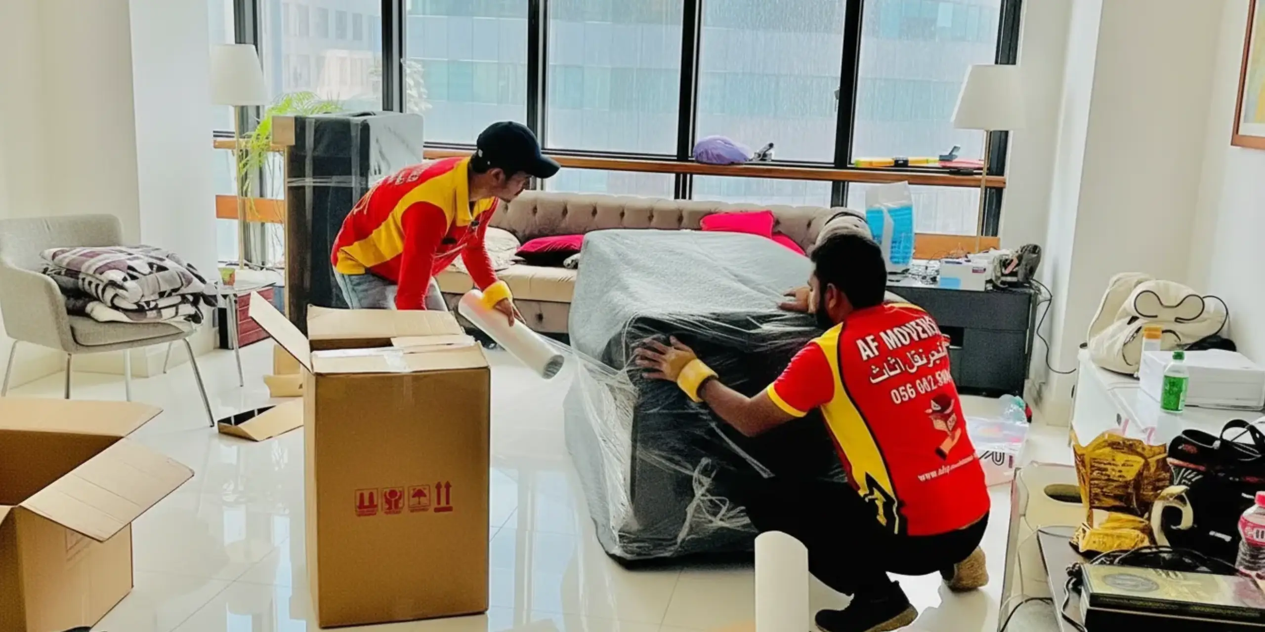 Al Fajer movers wrapping a sofa in protective film inside an Abu Dhabi apartment